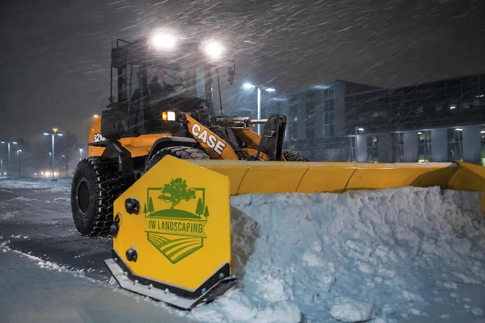 JW Landscaping CASE loader with a branded snow pusher plowing a commercial parking lot at night in Northern Kentucky