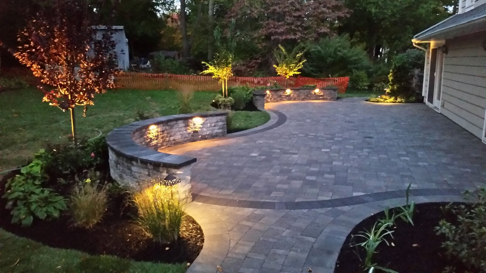 Paver patio with fire pit, seating wall, and landscape lighting by JW Landscaping