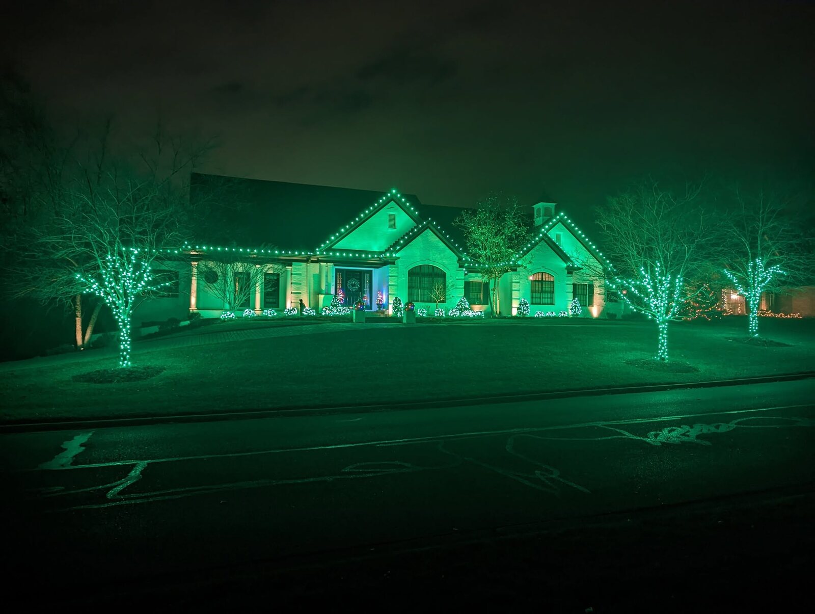 Home with green Christmas lighting and wrapped trees by JW Landscaping