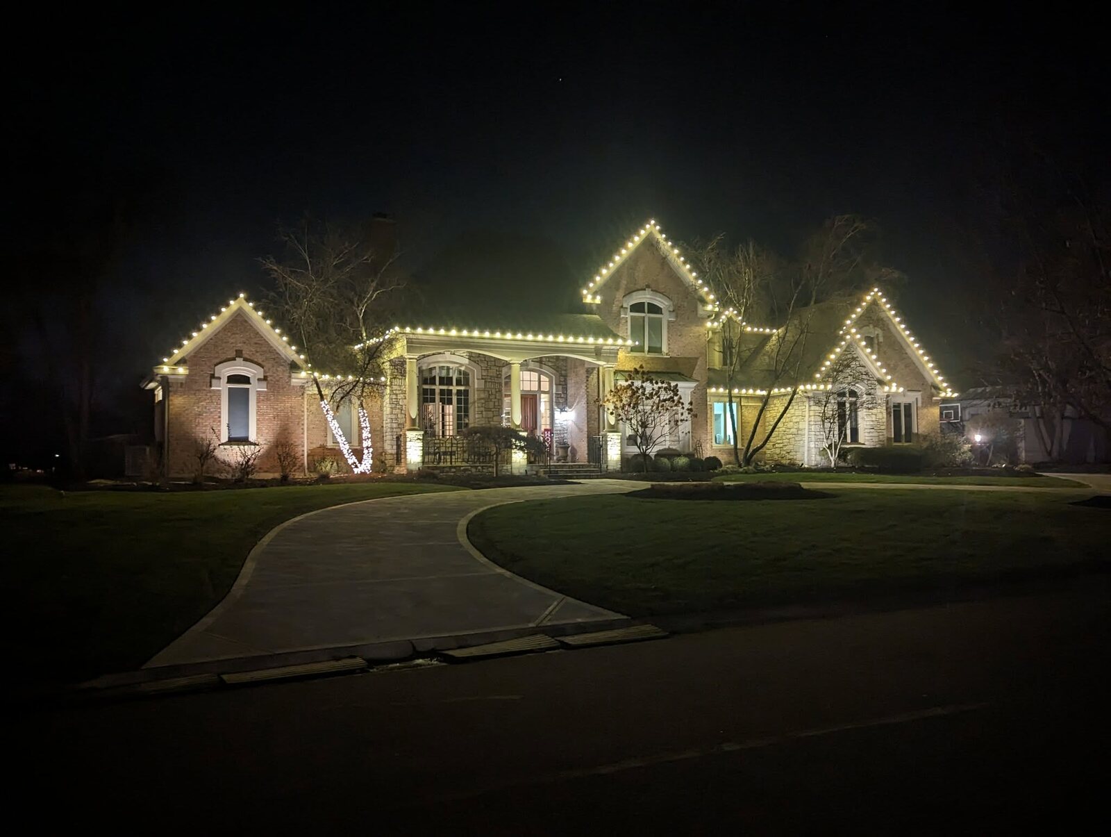 Brick home with warm white Christmas roofline lights by JW Landscaping