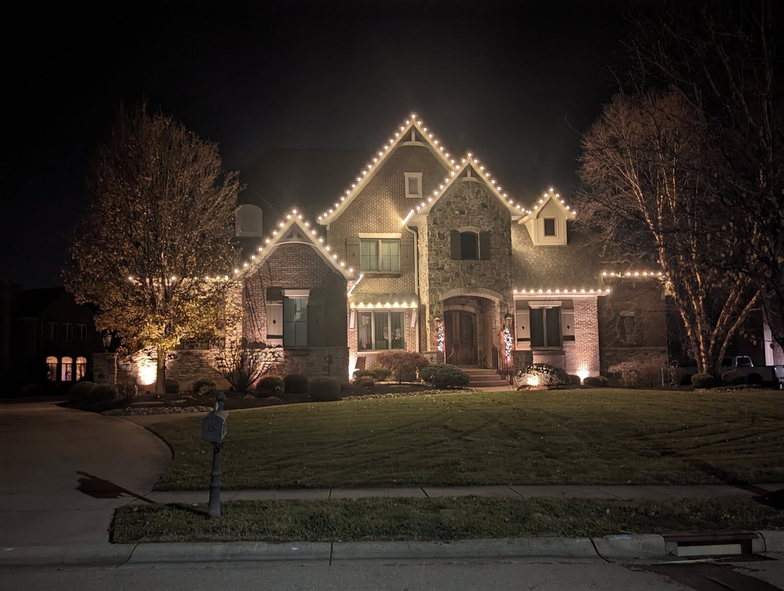 Home with peaked-roof Christmas lighting and uplighting by JW Landscaping