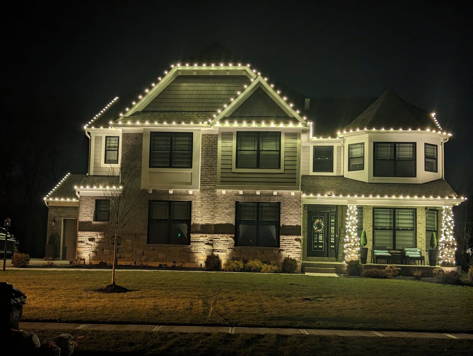 Two-story home with Christmas lights and wrapped trees by JW Landscaping